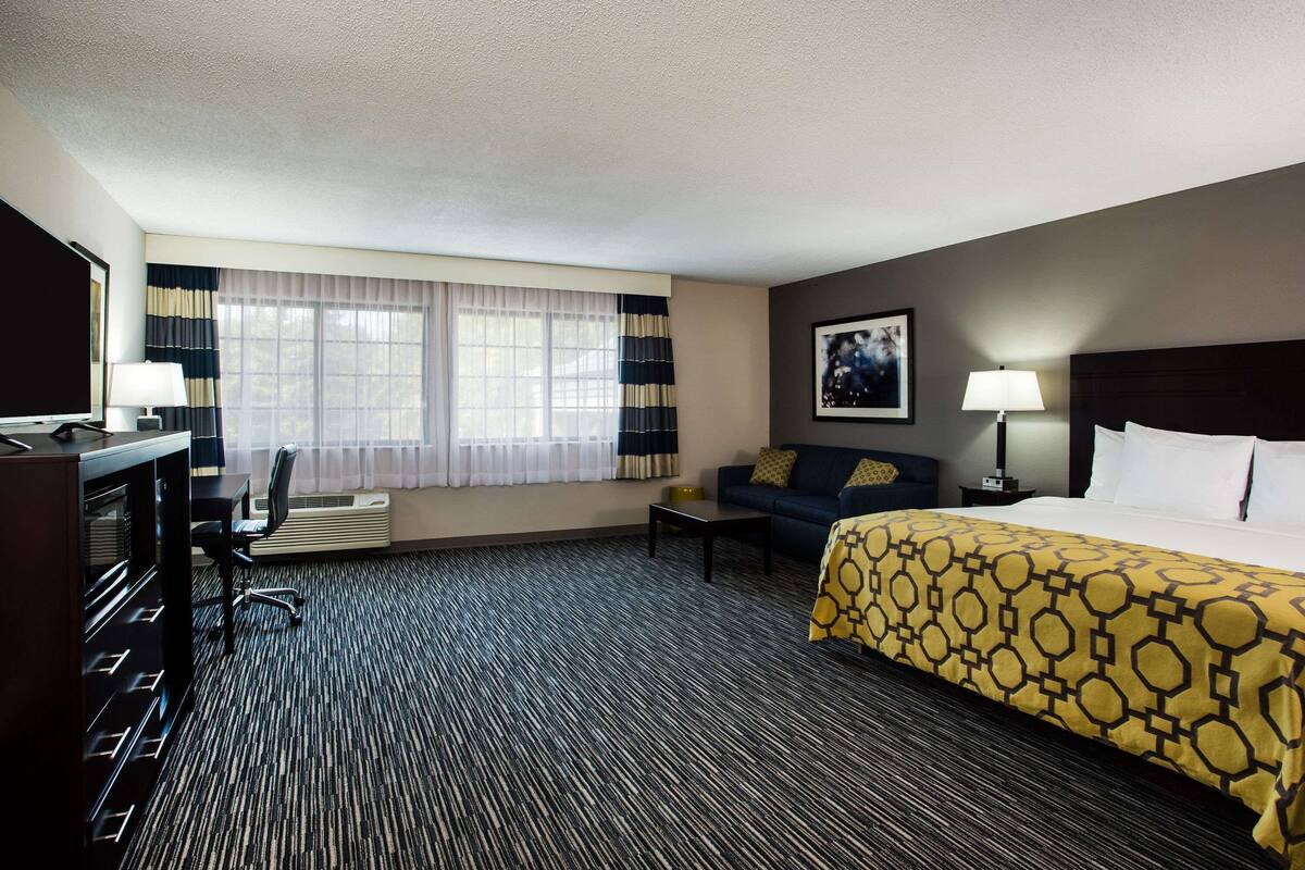 A hotel room with a large bed, a desk, a chair, a sofa, and a window with curtains.