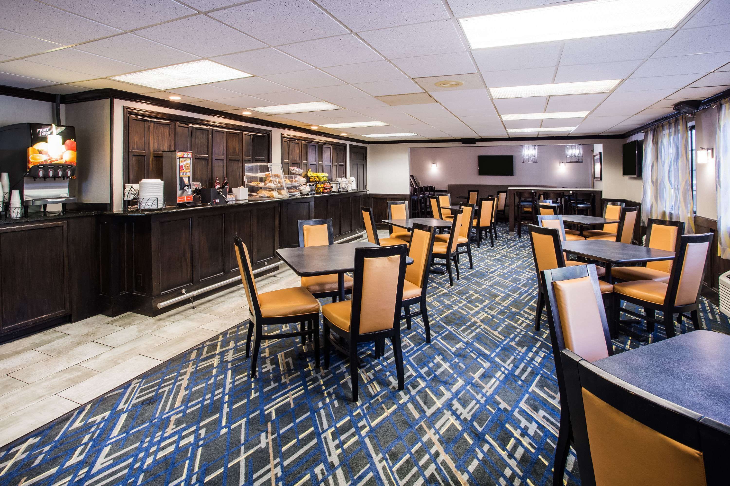 Un comedor de hotel con bar, varias mesas y sillas, y una alfombra estampada.