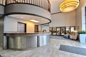 A modern reception area with a curved counter, a staircase, and a seating area with a large potted plant.