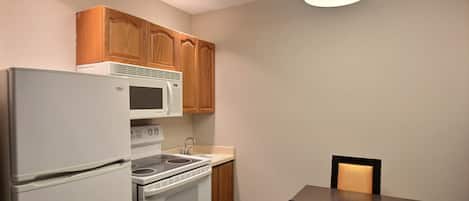 Una cocina compacta con refrigerador, microondas, estufa y armarios de madera.