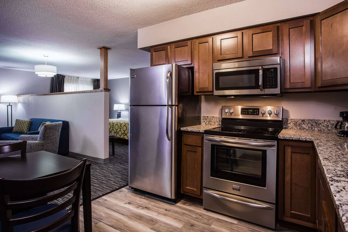 A compact kitchen with stainless steel appliances, wooden cabinets, and a granite countertop.