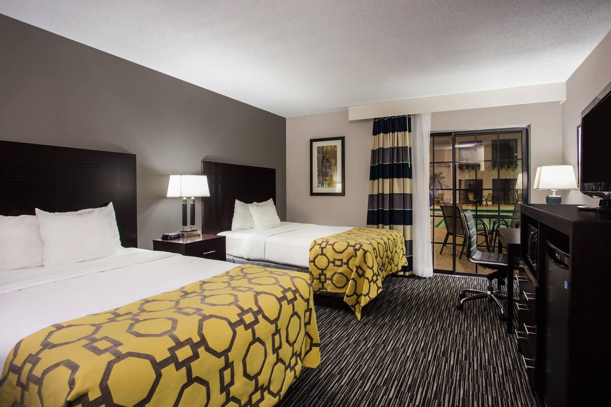 A hotel room with two beds, a desk with a chair, a TV, and a window with curtains.