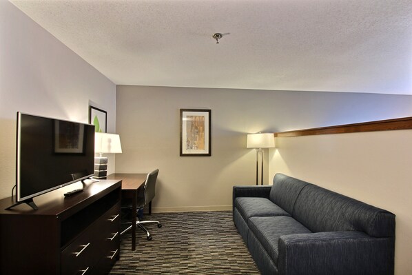 A hotel room with a flat-screen TV, a desk with a chair, a sofa, and two wall-mounted lamps.