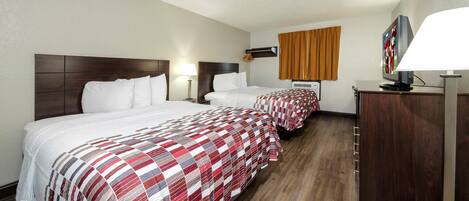 A hotel room with two beds, a wooden headboard, a flat-screen TV, a desk, and a wardrobe.