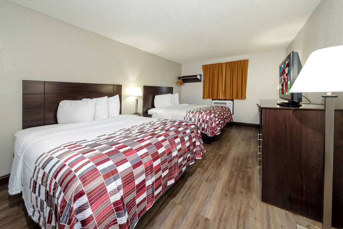 A hotel room with two beds, a wooden floor, a TV on a stand, and a lamp.