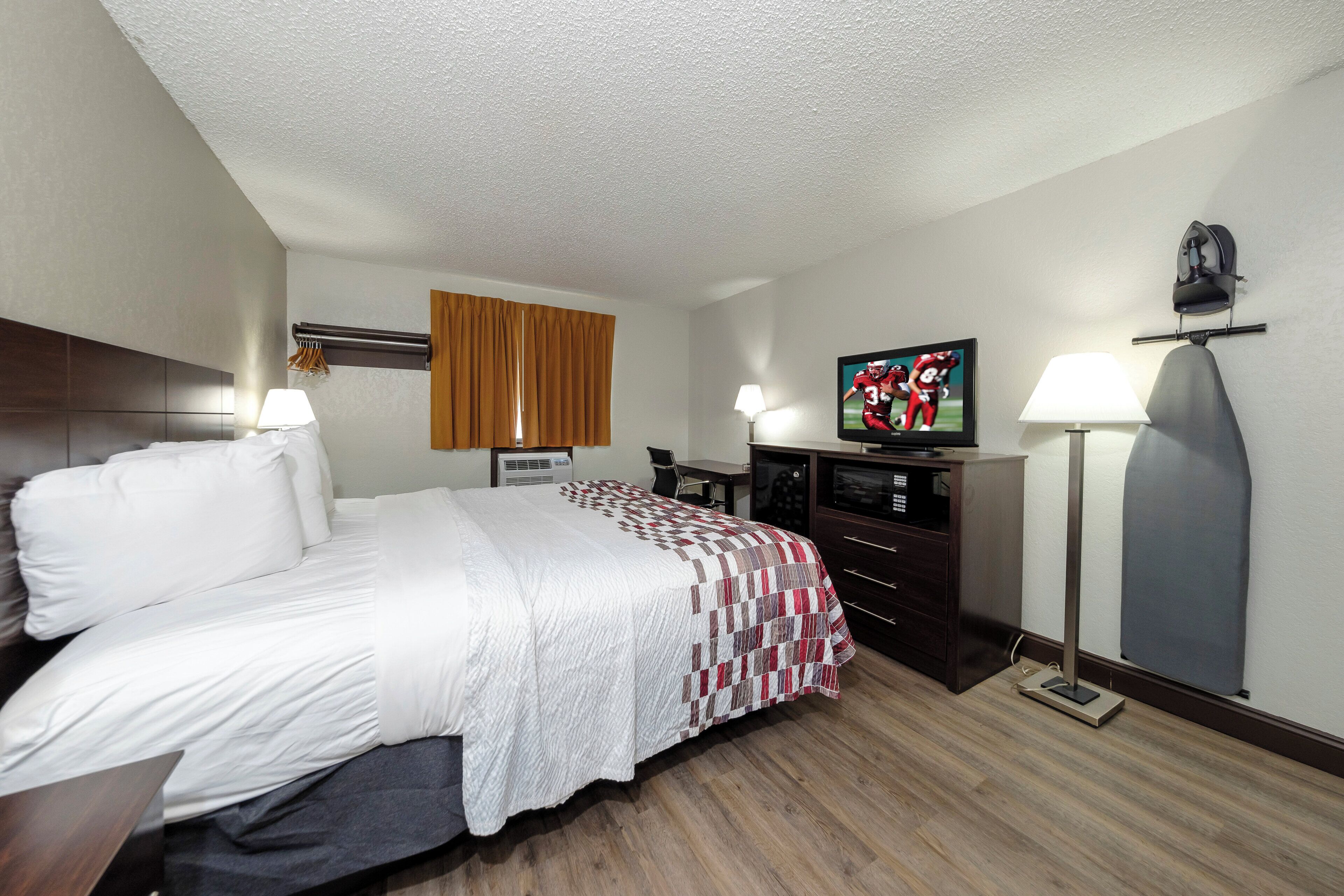 A hotel room with a bed, a television, a desk, and a lamp.