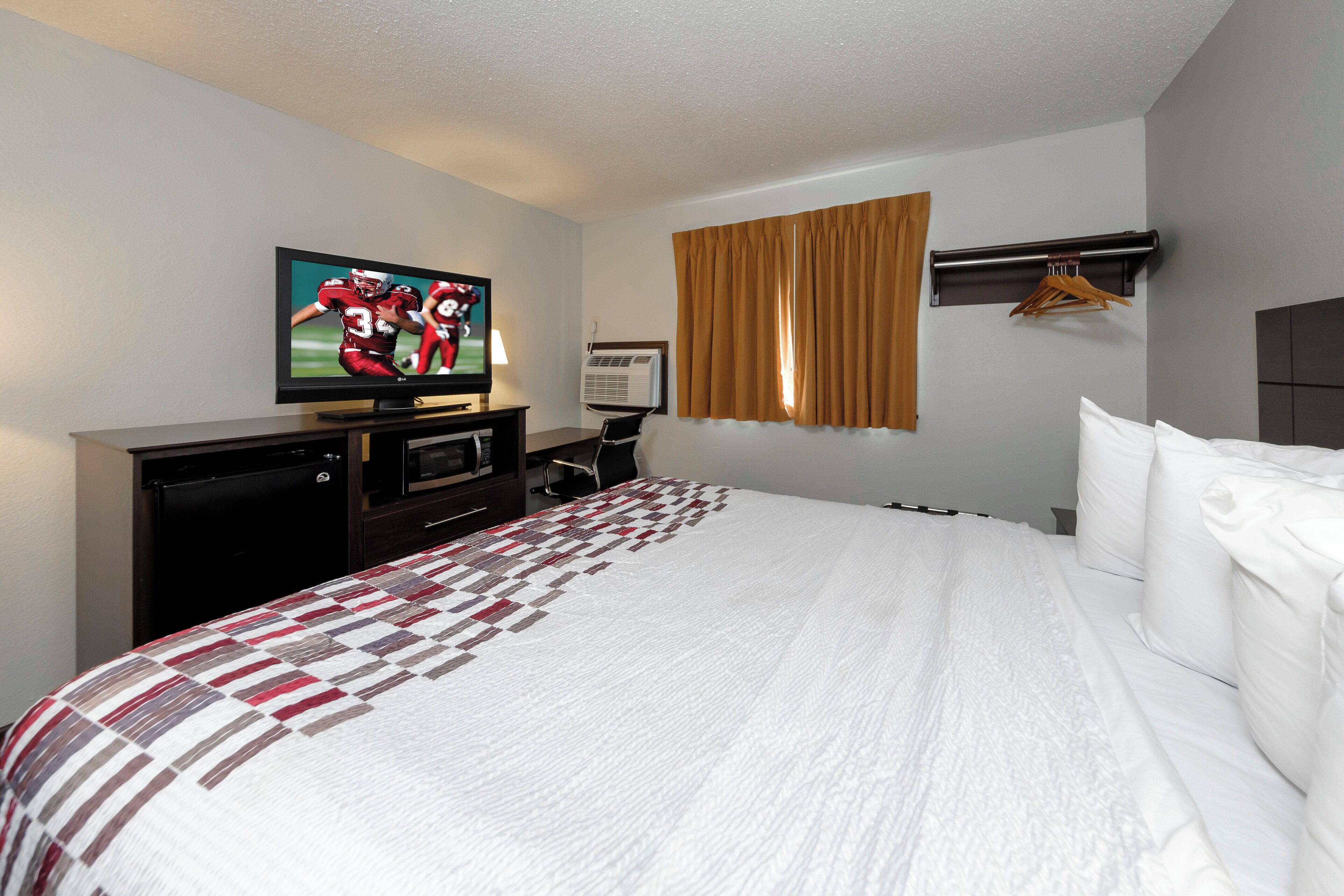 Una habitación de hotel con cama, televisión, escritorio y aire acondicionado instalado en la pared.