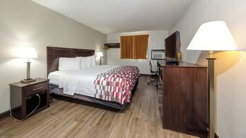 Une chambre d’hôtel comprenant un lit, une table de chevet, une lampe, un bureau avec une chaise et un téléviseur.