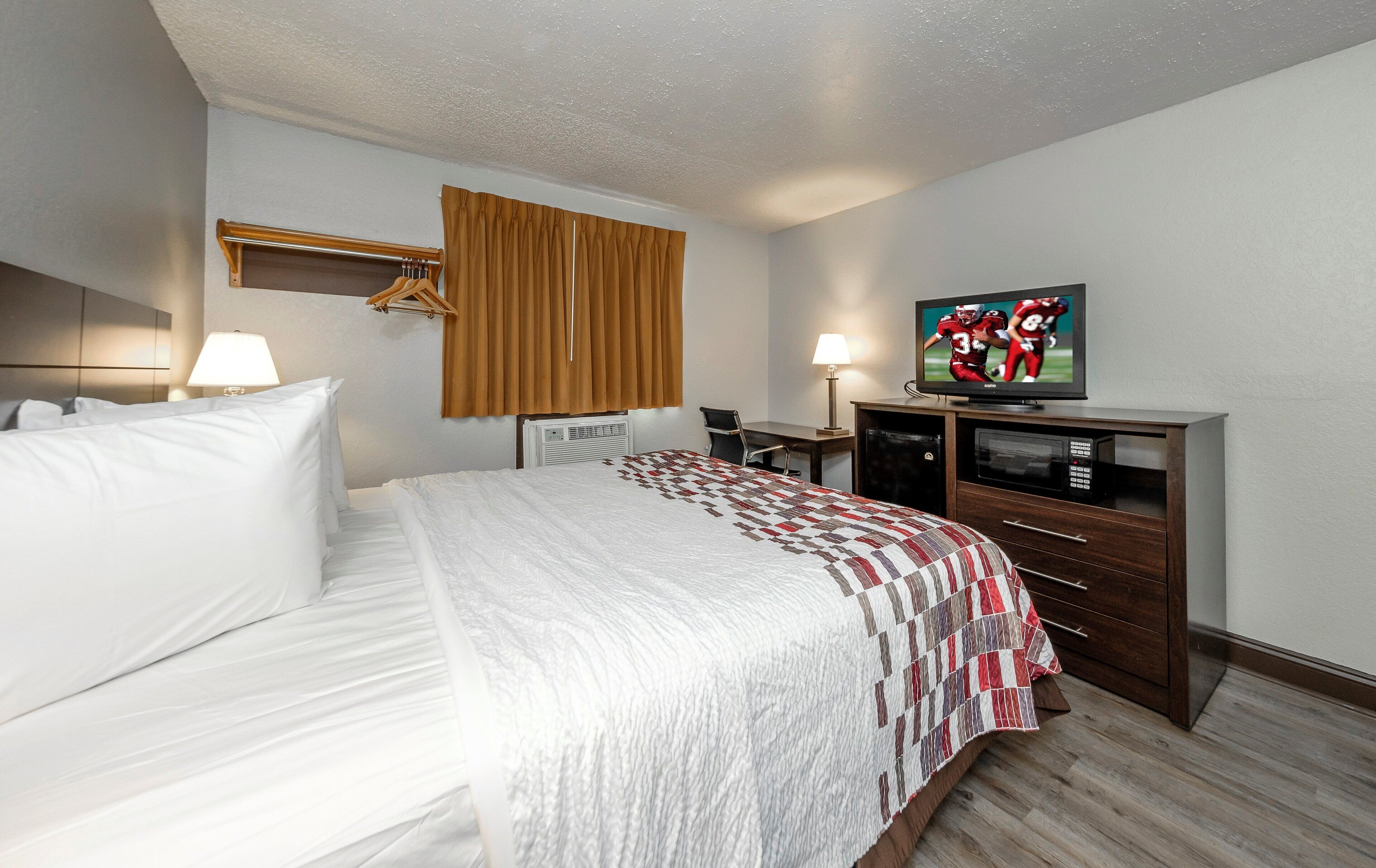 A hotel room with a bed, a desk, a television, and a window with curtains.