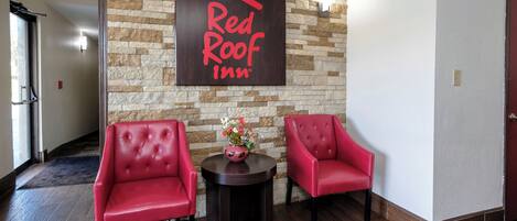 A Red Roof Inn lobby with two red leather chairs, a small table with a vase, and a stone wall with a sign.