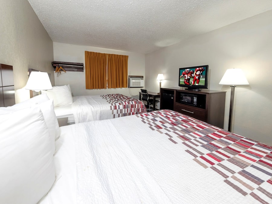 Habitación de hotel con dos camas, televisión, escritorio y ventana con cortinas.
