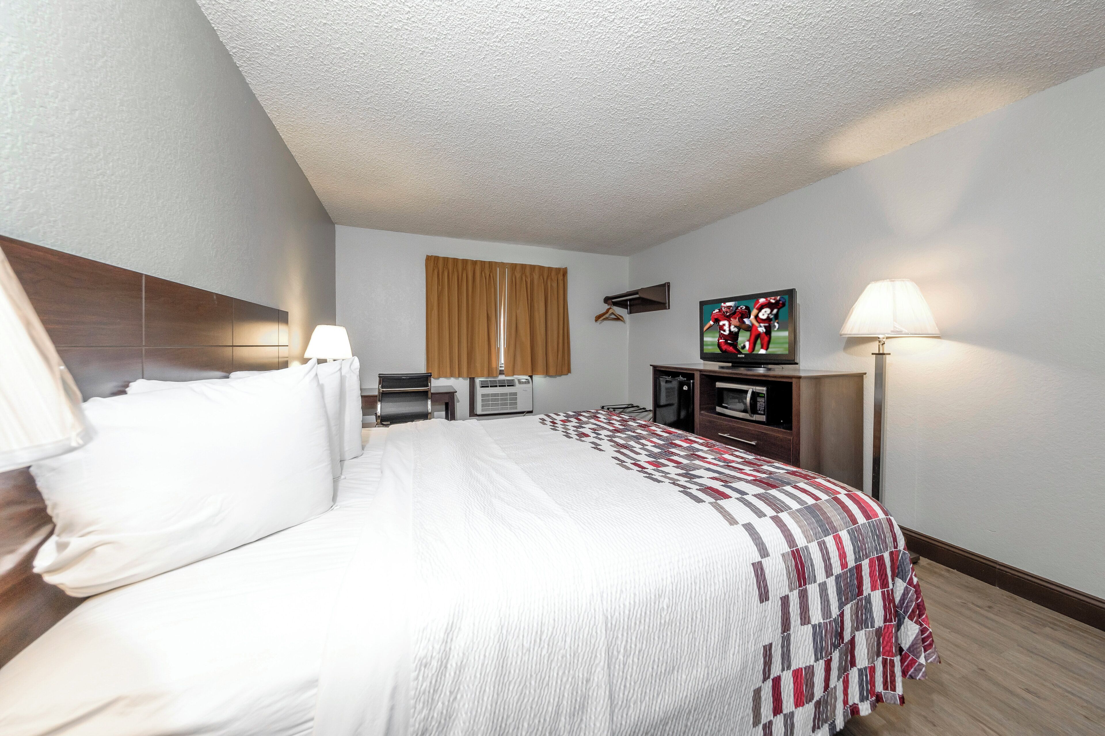 A hotel room with a bed, a TV, a desk, and a lamp.