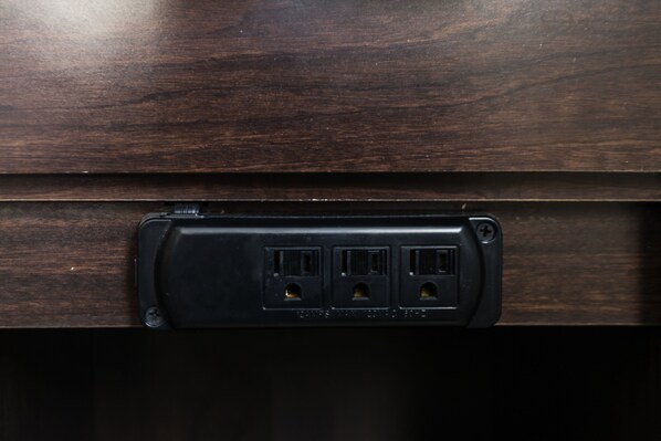 Un panneau en bois foncé avec une boîte de prise électrique noire contenant trois prises et un port USB.