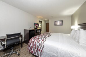 Une chambre d’hôtel avec un lit, un bureau équipé d’un ordinateur, une chaise, une lampe de bureau et un tableau encadré au mur.
