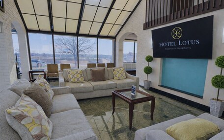A hotel lobby with a large window, a sofa set, a coffee table, and a sign reading "HOTEL LOTUS Essence in Hospitality".