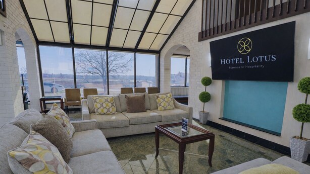 Un hall d’hôtel doté d’une grande fenêtre, d’un ensemble de canapés, d’une table basse et d’une enseigne indiquant : « HÔTEL LOTUS, l’essence de l’hospitalité ».