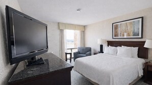 Une chambre d’hôtel avec un lit, une télévision, une chaise, une lampe et un tableau au mur.
