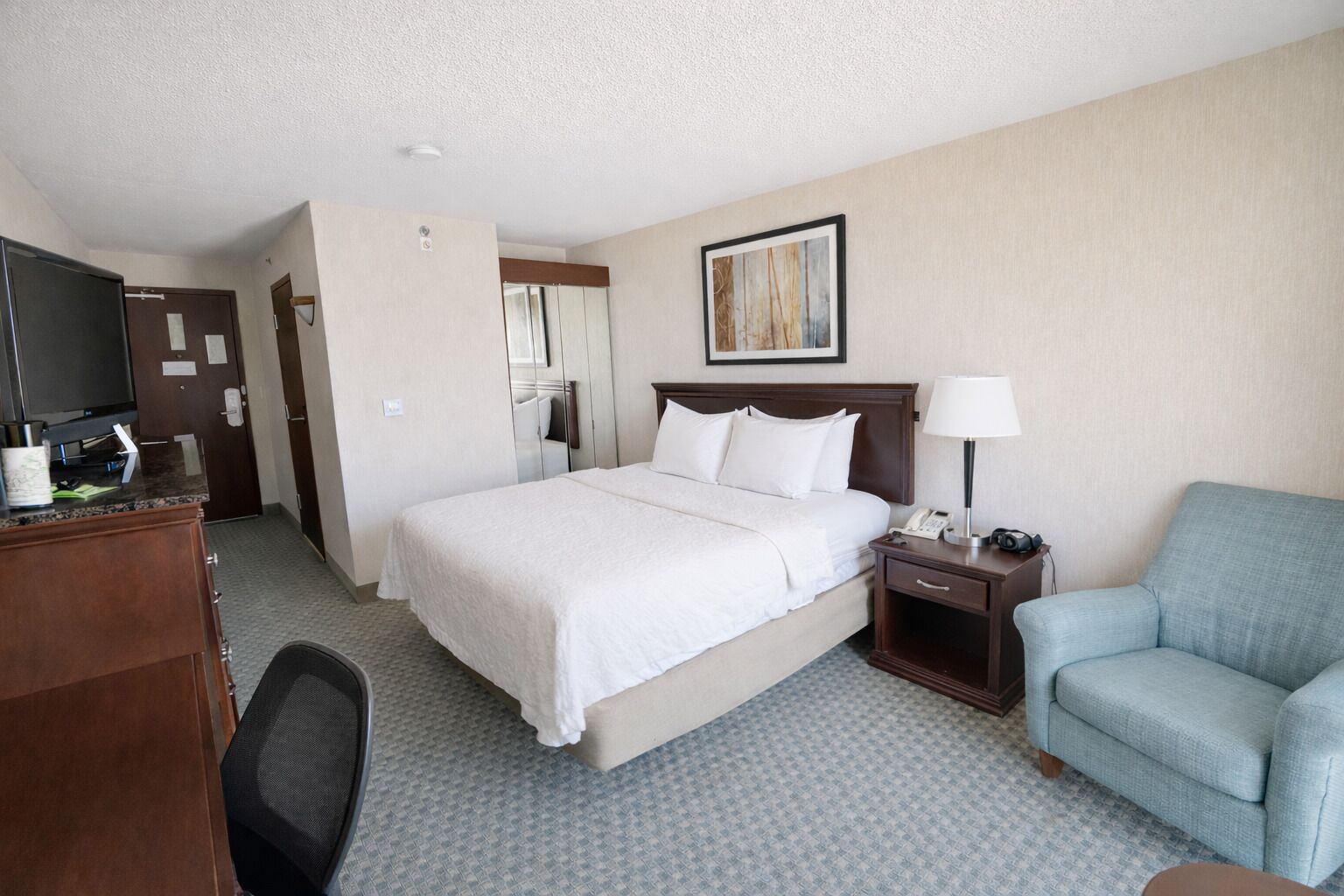 A hotel room with a bed, a desk with a computer, a chair, and a TV.