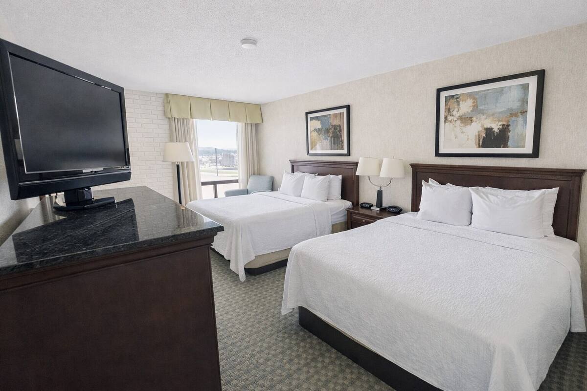 A hotel room with two beds, a TV, a desk, and a window with a view.