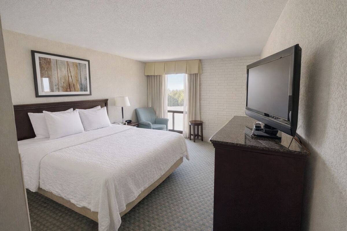 A hotel room with a large bed, a television, a chair, and a small table.