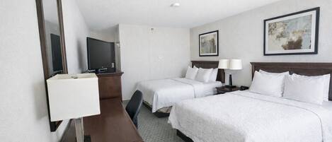 A hotel room with two beds, a desk with a chair, a TV, and two bedside tables with lamps.