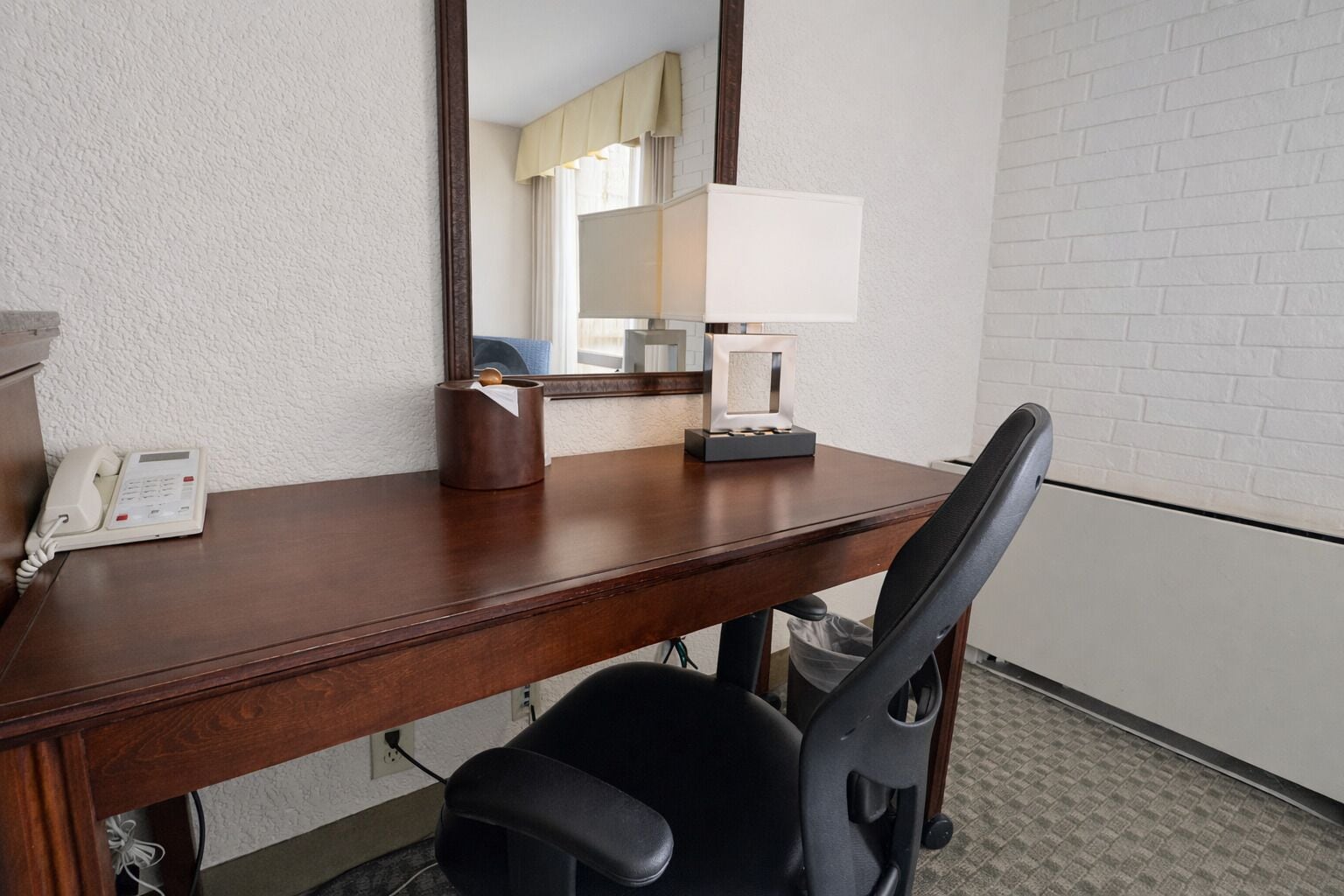 A hotel room with a wooden desk, a telephone, a tissue box, a lamp, and a chair.