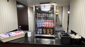 Un espace d’accueil d’hôtel comprenant un distributeur de boissons en libre-service, un plateau de bouteilles d’eau et une machine à café.