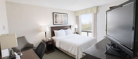 A hotel room with a bed, a desk, a chair, a TV, and a window with curtains.