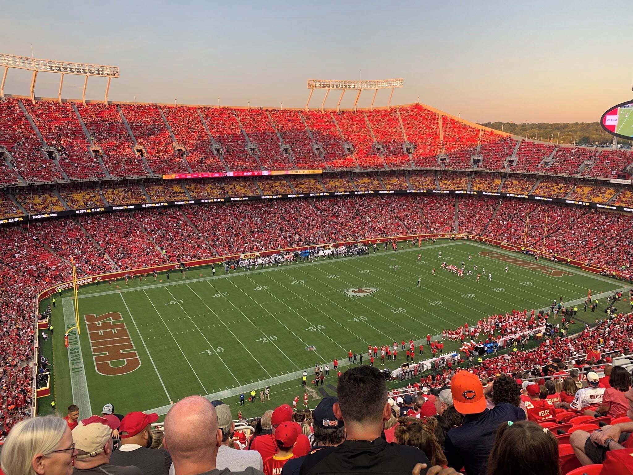 A stadium filled with spectators, featuring tiered seating and a football field.