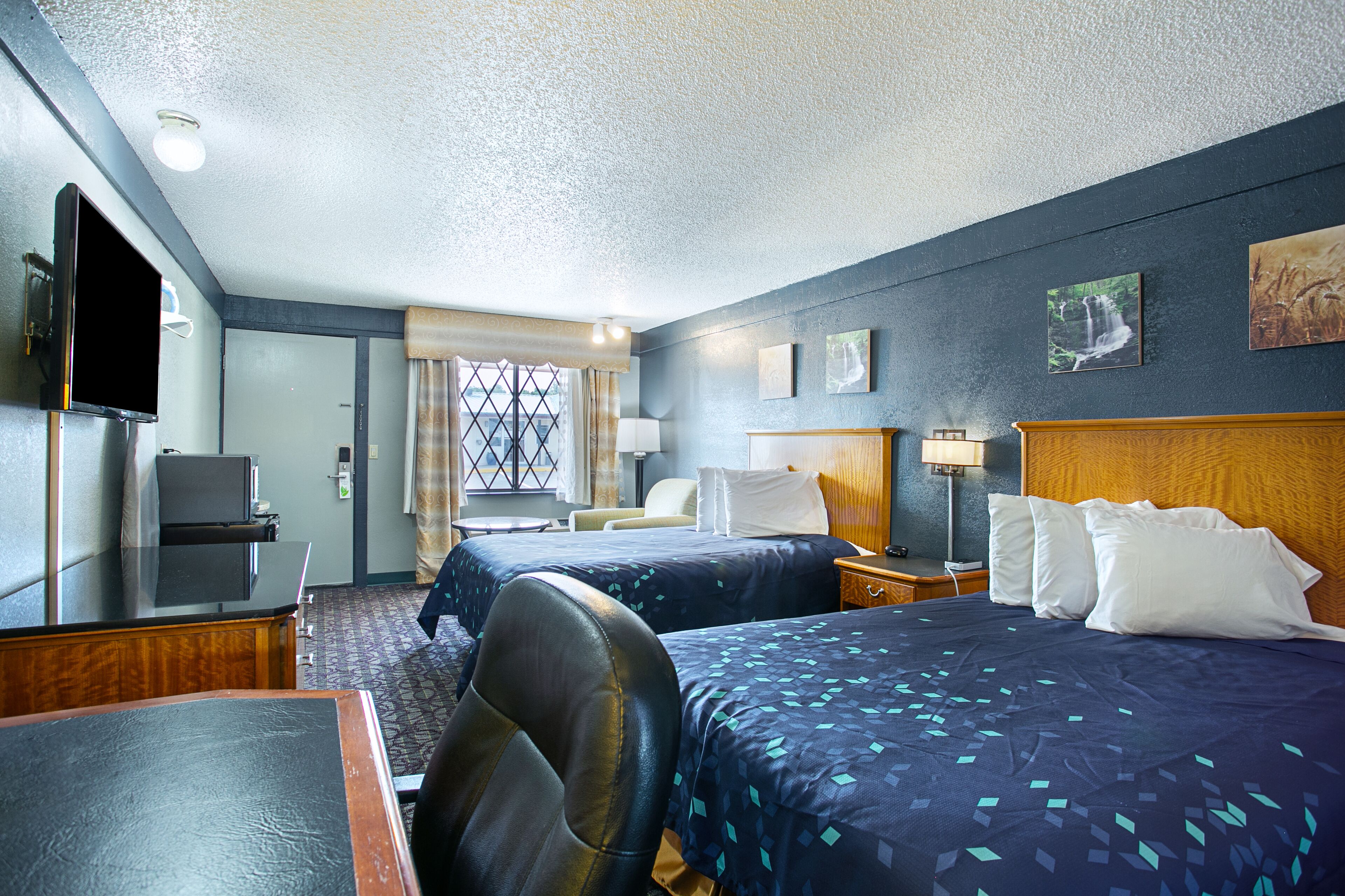 A hotel room with two beds, a desk, a TV, and a window with curtains.