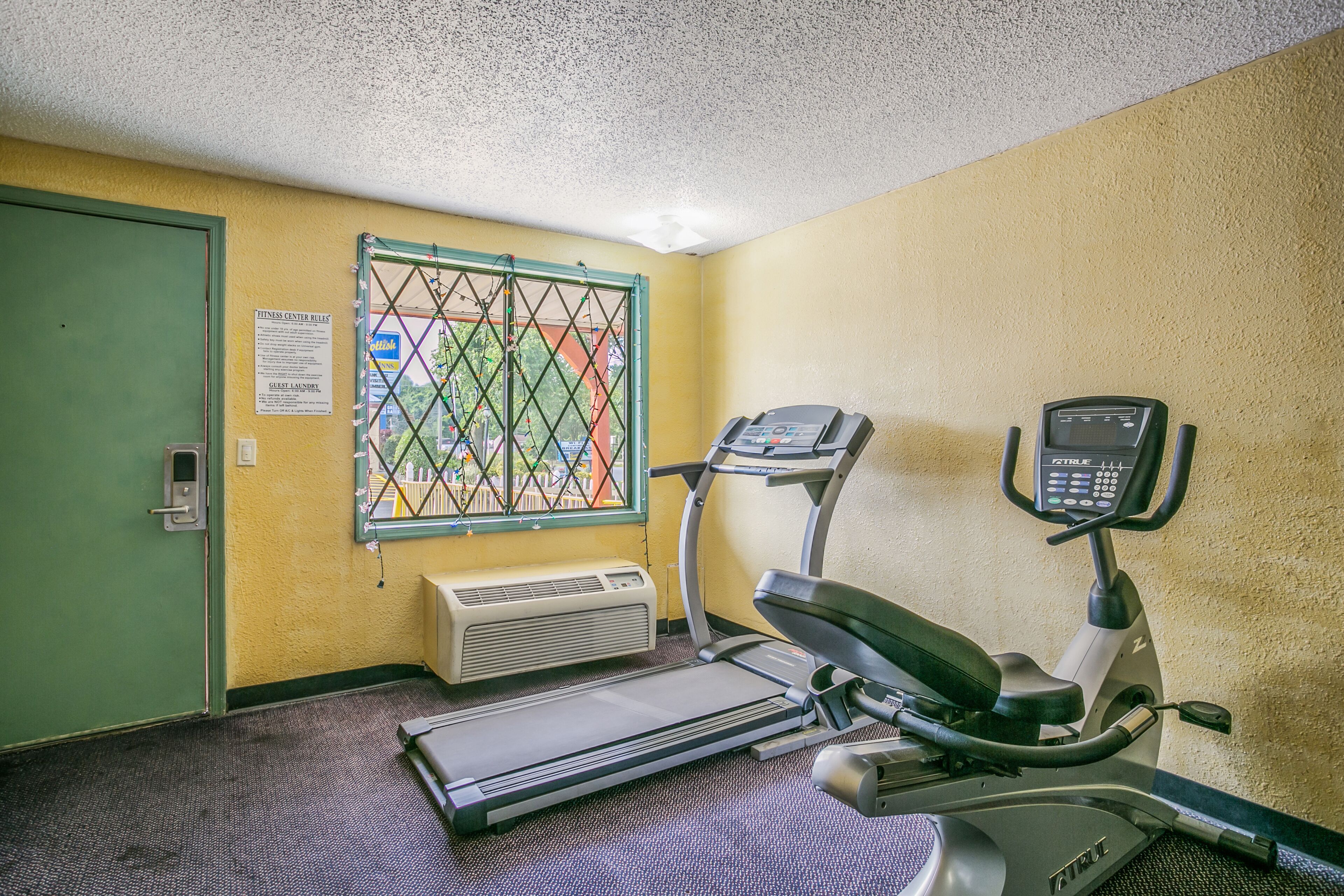 A fitness center with a treadmill, stationary bike, and air conditioning unit.