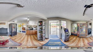 Una habitación amplia con suelo de madera, alfombra azul, sofá, una mesa de centro y un refrigerador.