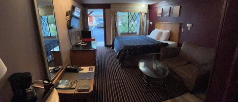 A hotel room with a bed, a desk with a computer, a TV, and a window with a view of the outside.