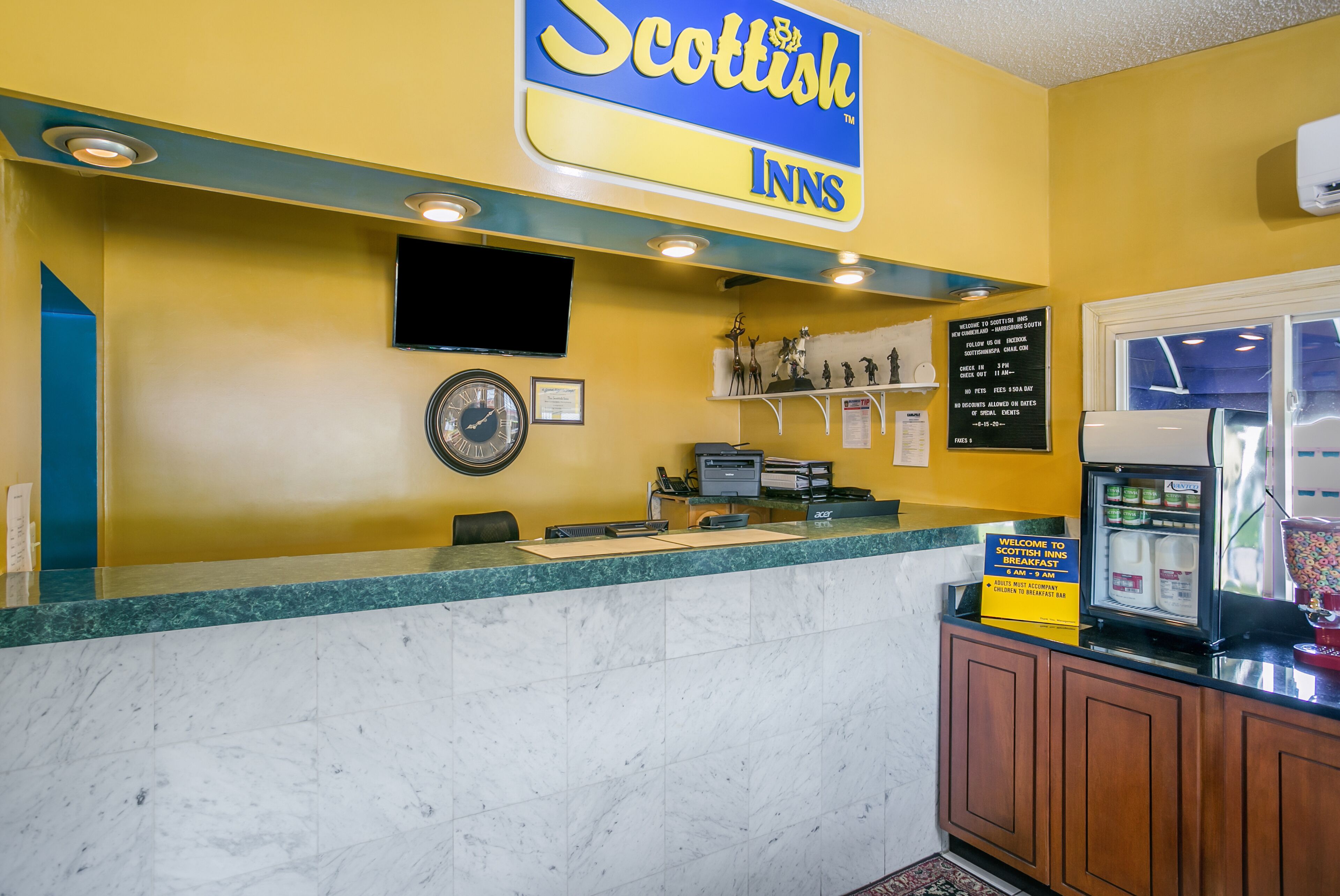 Une salle d’attente avec un mur jaune, une horloge, un téléviseur et une machine à café.