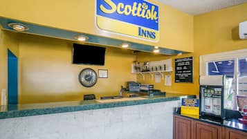 Une salle d’attente avec un mur jaune, une horloge, un téléviseur et une machine à café.