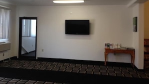 A room with a flat-screen TV mounted on the wall, a small wooden table with items on it, and a patterned carpet. - Motel 6 Sedalia, MO (Sedalia)