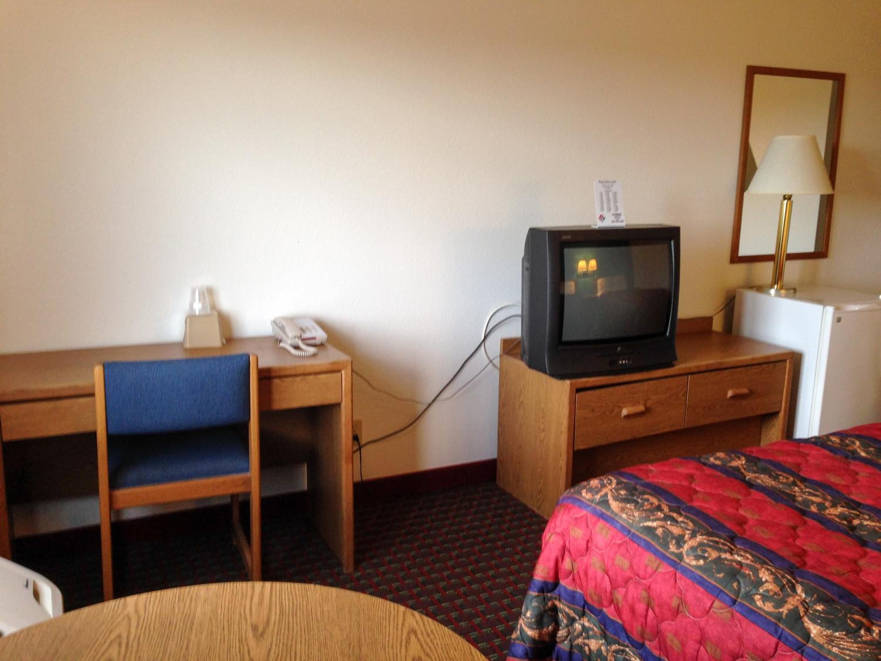 Ett hotellrum med ett skrivbord i trä, en stol, en tv, en lampa och en säng med ett mönstrat överkast.