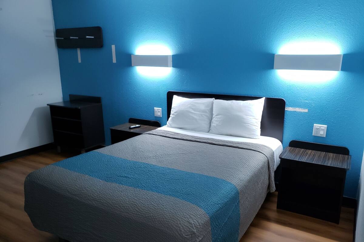 A neatly arranged hotel room with a bed, bedside tables, a dresser, and wall-mounted lights.