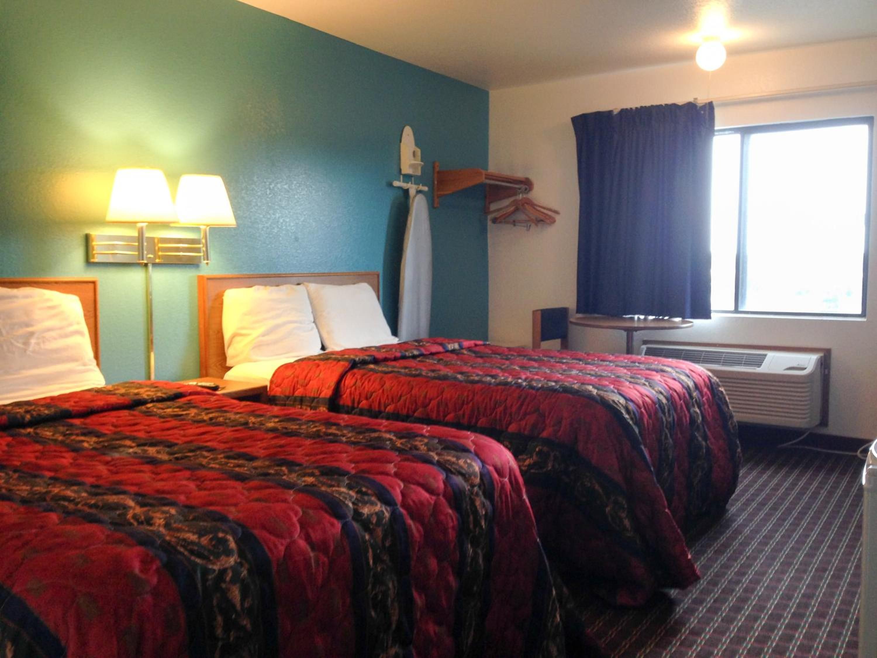 Hotelkamer met twee bedden, een bureau, een stoel, een raam met gordijnen en een airconditioning.