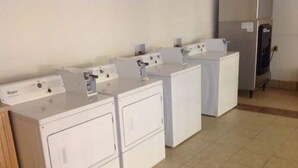 A laundry area with three front-loading washing machines and a refrigerator. - Motel 6 Sedalia, MO (Sedalia)