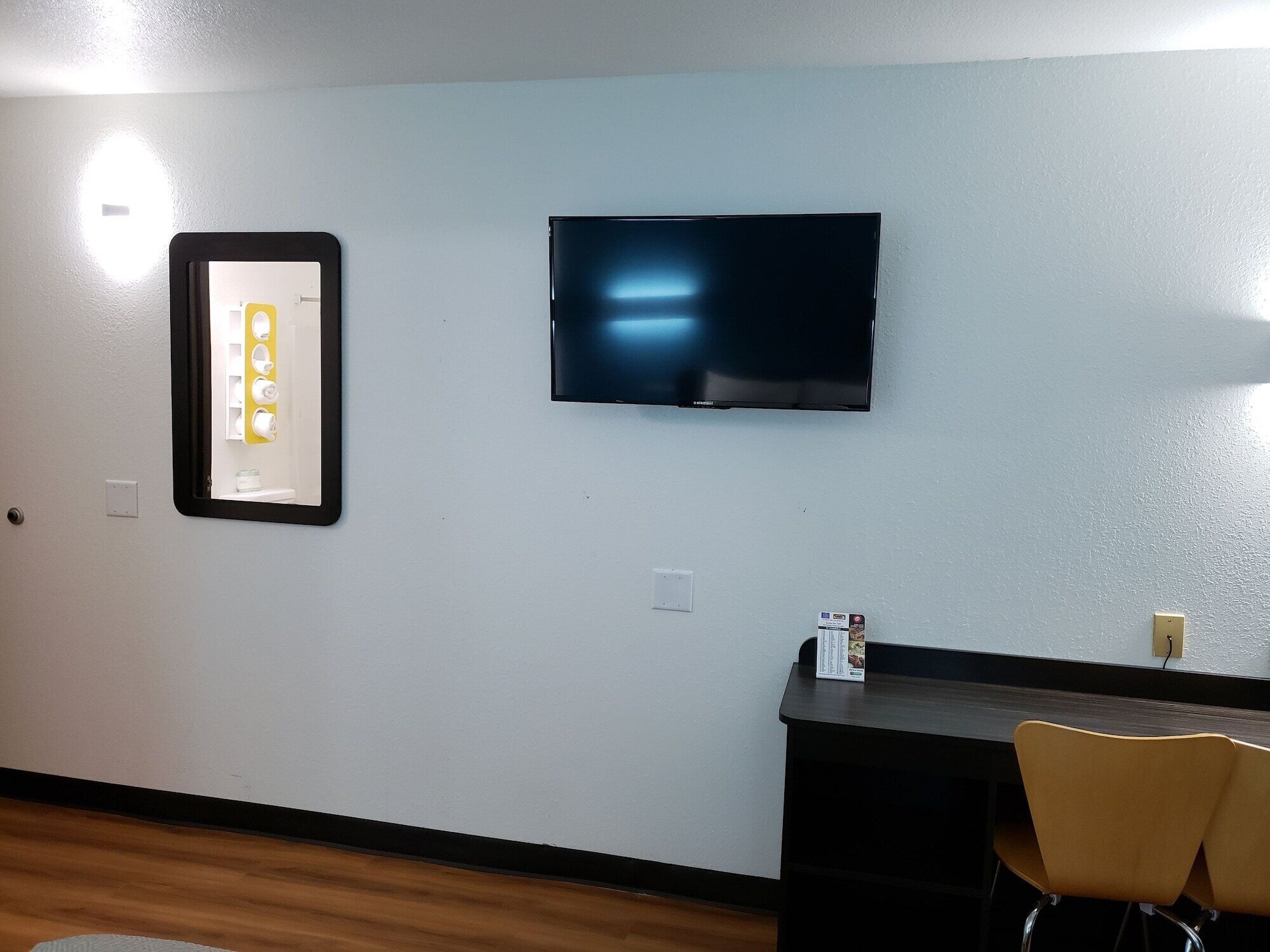 A room with a flat-screen TV mounted on the wall, a small table, and two chairs.