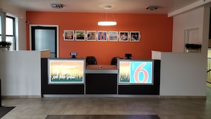 A reception desk with a large illuminated sign displaying the number '6'. - Motel 6 Sedalia, MO (Sedalia)