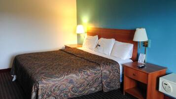 A hotel room with a bed, a nightstand, a lamp, and a control panel.