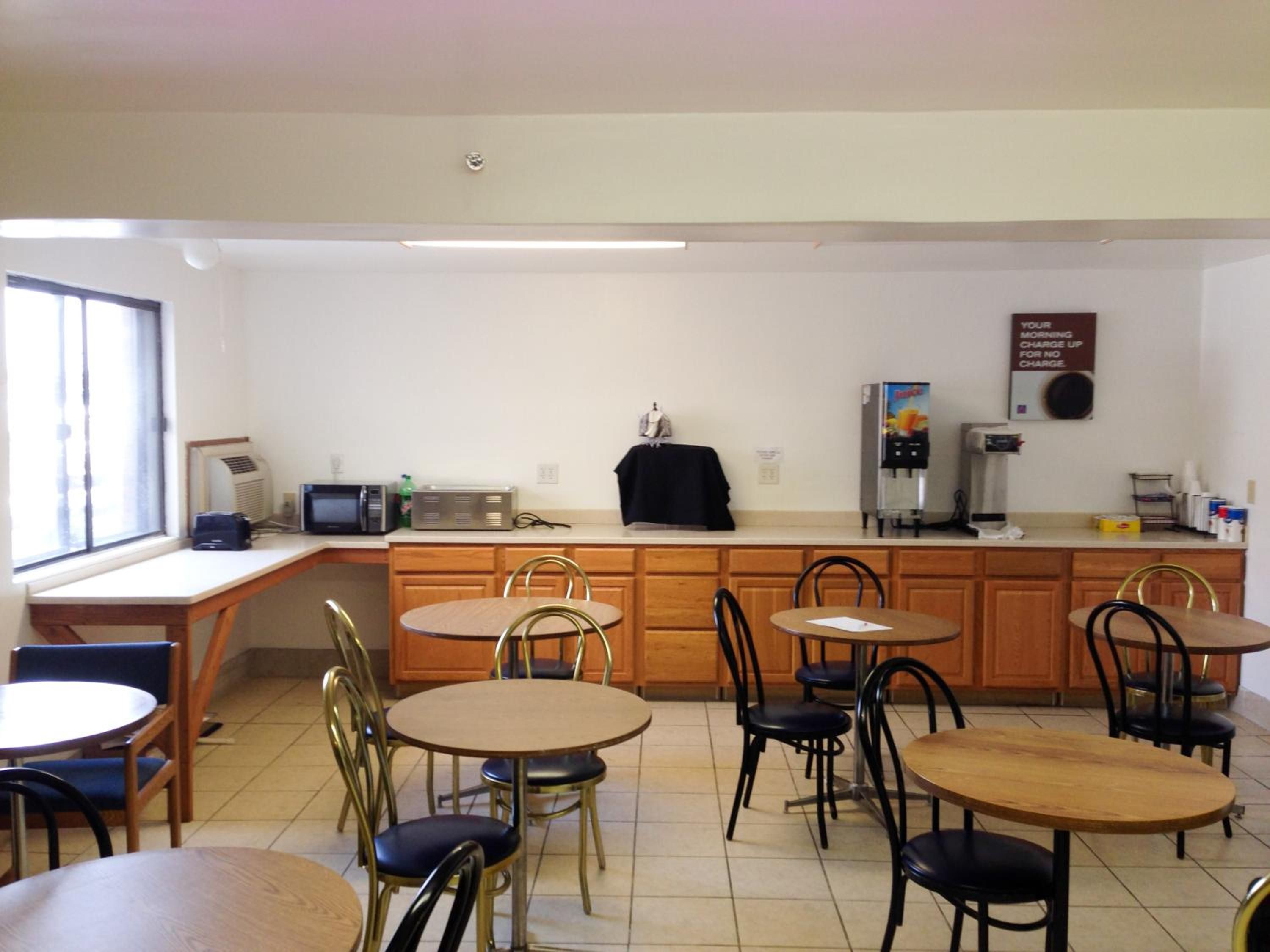 A small kitchenette with a microwave, toaster, and coffee maker. There are four wooden tables with chairs, and a window providing natural light.