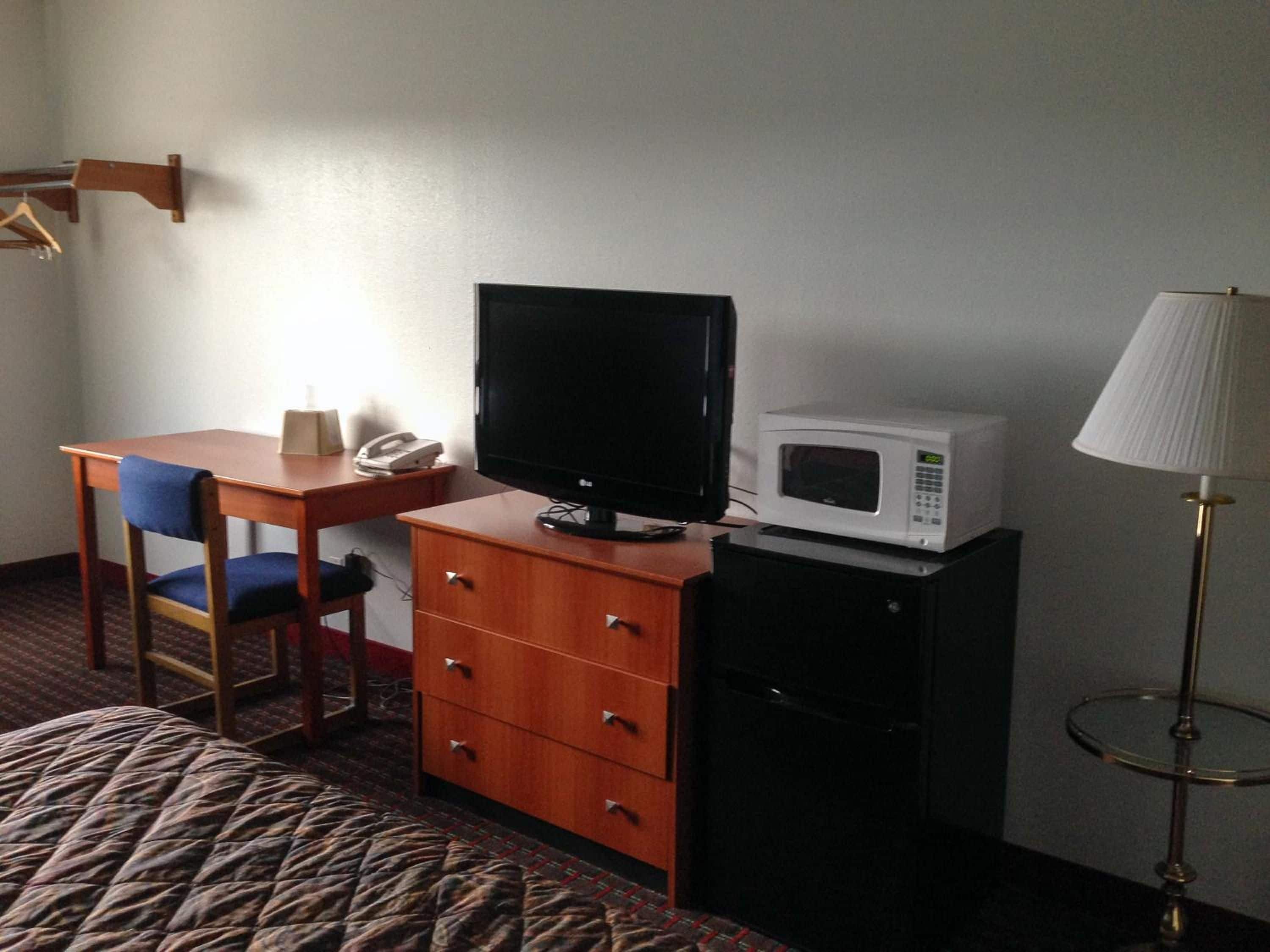 Ein Hotelzimmer mit einem Bett, einem Schreibtisch mit Stuhl, einem Fernseher, einer Mikrowelle, einem Schrank und einer Lampe.