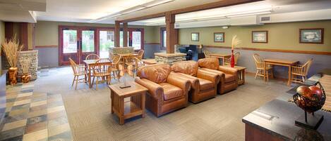 A spacious lobby with leather sofas, wooden tables, and chairs, a stone accent wall, and framed artwork on the walls.