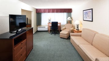 A hotel room with a TV, a desk, a chair, a sofa, and a lamp.