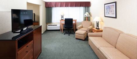 Quarto de hotel com televisão, escrivaninha, cadeira, sofá e abajur.