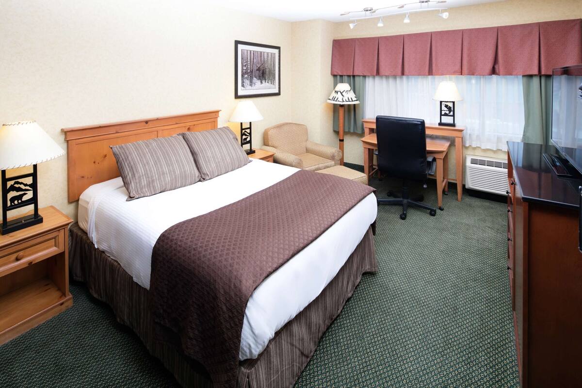 A hotel room with a large bed, a desk, a chair, and a TV.