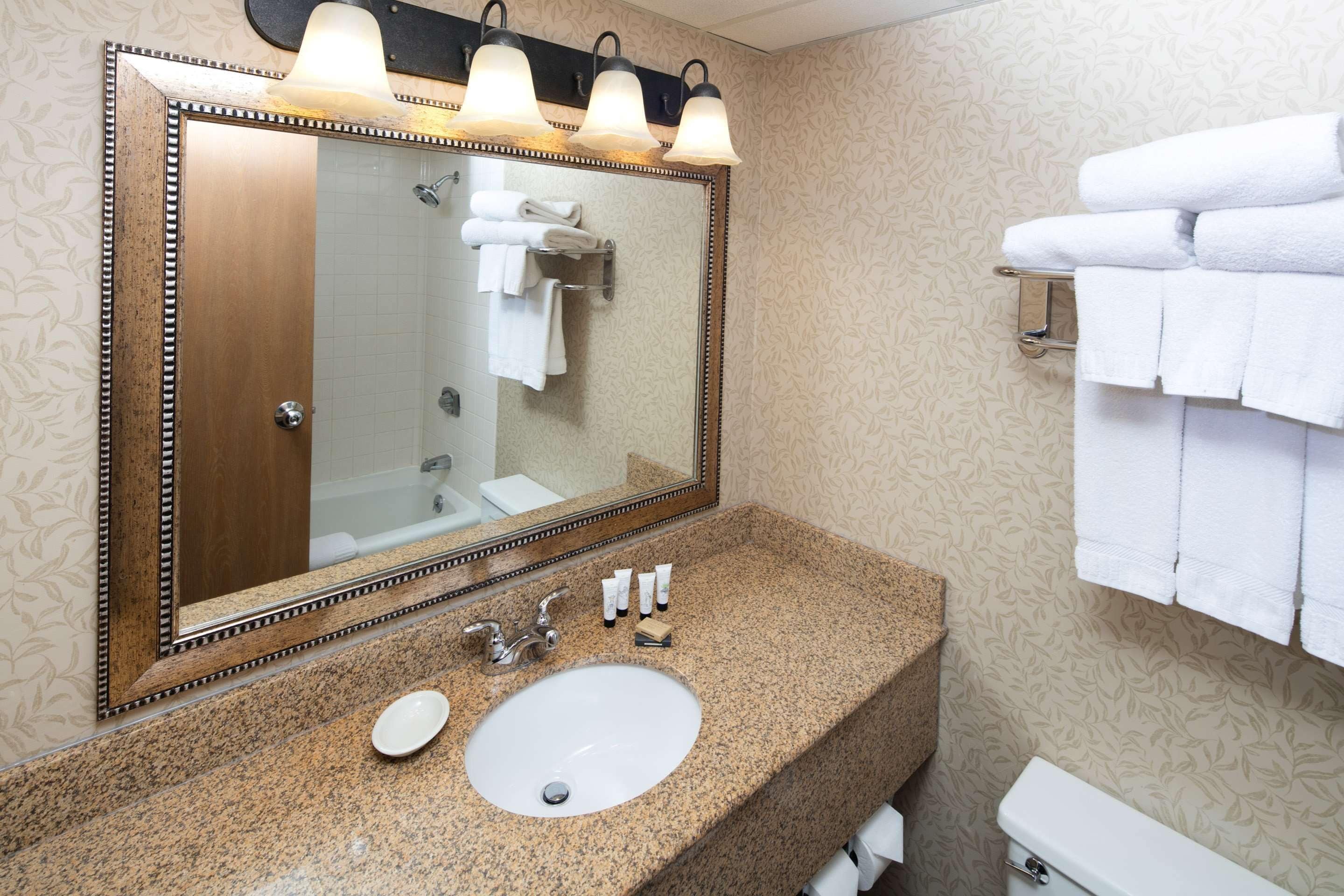 Une salle de bain avec un comptoir en granit, un lavabo blanc, un grand miroir avec éclairage intégré et un porte-serviettes.